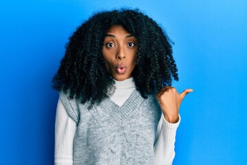 African american woman with afro hair wearing casual winter sweater surprised pointing with hand finger to the side, open mouth amazed expression.