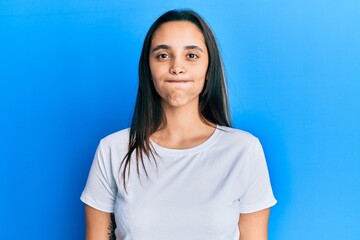 Young hispanic woman wearing casual white t shirt puffing cheeks with funny face. mouth inflated with air, crazy expression.