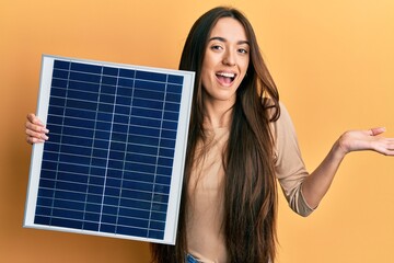 Young hispanic girl holding photovoltaic solar panel celebrating achievement with happy smile and winner expression with raised hand