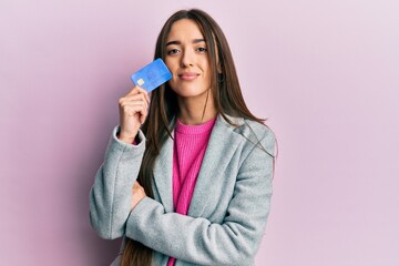 Young hispanic girl holding credit card relaxed with serious expression on face. simple and natural looking at the camera.