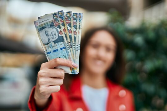 Young hispanic woman smiling happy holding peruvian sol banknotes at the city.