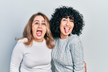 Middle east mother and daughter wearing casual clothes sticking tongue out happy with funny expression. emotion concept.