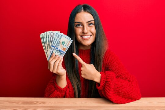 Beautiful hispanic woman holding dollars smiling happy pointing with hand and finger