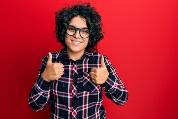 Young hispanic woman with curly hair wearing casual clothes and glasses success sign doing positive gesture with hand, thumbs up smiling and happy. cheerful expression and winner gesture.