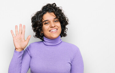 Young hispanic woman with curly hair wearing casual clothes waiving saying hello happy and smiling, friendly welcome gesture