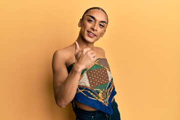 Hispanic man wearing make up and long hair wearing womans top doing happy thumbs up gesture with hand. approving expression looking at the camera showing success.