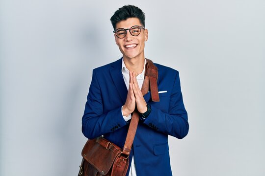 Young hispanic man wearing business clothes praying with hands together asking for forgiveness smiling confident.