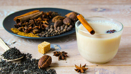 Traditional indian drink - masala tea with spices wooden background. Close up popular Indian or Asian traditional drink with spices and sugar. Spice tea with different ingredients in a glass cup.