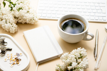 Beige and white work space with coffee cup, notepad and lilac flowers