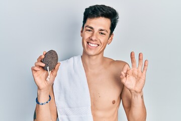 Young hispanic man naked holding pumice stone doing ok sign with fingers, smiling friendly gesturing excellent symbol