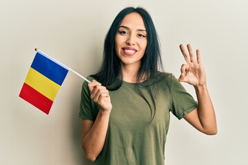 Young hispanic girl holding romania flag doing ok sign with fingers, smiling friendly gesturing...