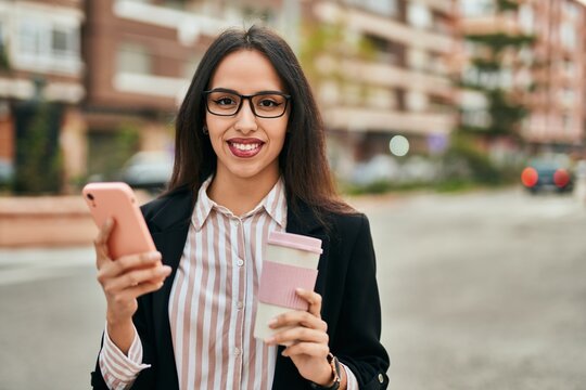 Young hispanic businesswoman using smartphone drinking coffee at the city.