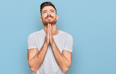 Young redhead man wearing casual grey t shirt begging and praying with hands together with hope...