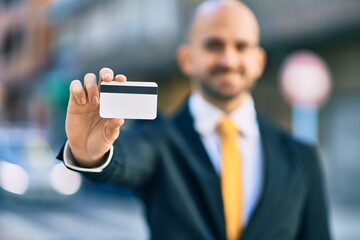 Young hispanic bald businessman smiling happy holding credit card at the city.
