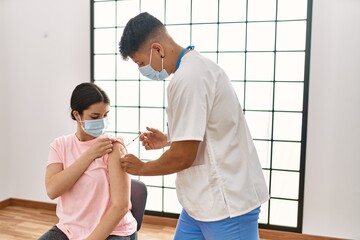 Young nurse man injecting covid-19 coronavirus vaccine for woman at the clinic.