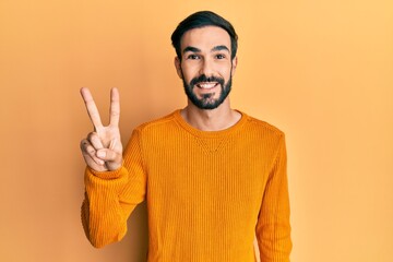 Young hispanic man wearing casual clothes showing and pointing up with fingers number two while smiling confident and happy.