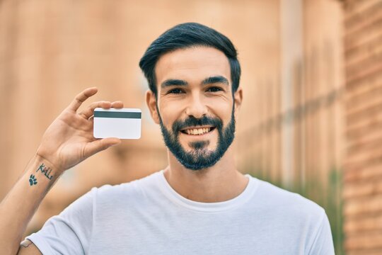 Young hispanic man smiling happy holding credit card at the city.