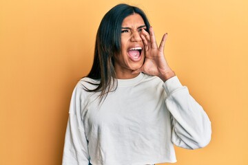 Young latin transsexual transgender woman wearing casual clothes shouting and screaming loud to side with hand on mouth. communication concept.