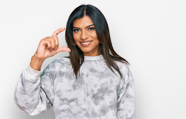 Young latin transsexual transgender woman wearing casual clothes smiling and confident gesturing with hand doing small size sign with fingers looking and the camera. measure concept.