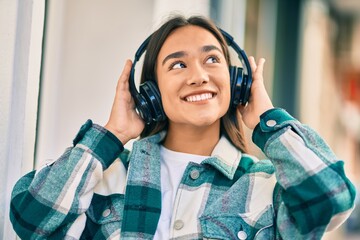 Young latin girl smiling happy using headphones at the city.