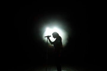 black silhouette of female singer with white spotlights in the background