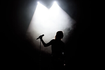 black silhouette of female singer with white spotlights in the background