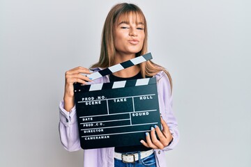 Teenager caucasian girl holding video film clapboard looking at the camera blowing a kiss being...