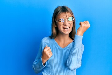 Teenager caucasian girl wearing casual clothes and glasses celebrating surprised and amazed for success with arms raised and eyes closed