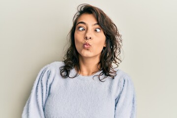 Young hispanic woman wearing casual winter sweater making fish face with lips, crazy and comical gesture. funny expression.