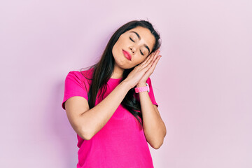 Young hispanic girl wearing casual pink t shirt sleeping tired dreaming and posing with hands together while smiling with closed eyes.