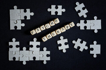 The word psychotherapy made up of letter cubes among puzzles on a dark surface. The concept of using psychotherapy methods in solving human mental problems