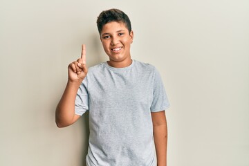 Teenager hispanic boy wearing casual grey t shirt showing and pointing up with finger number one...