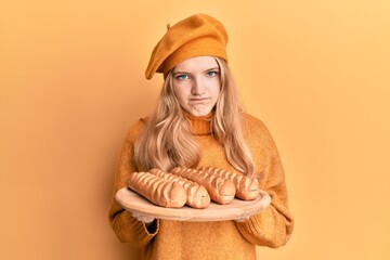 Beautiful young caucasian girl wearing french look with beret holding baguettes bread skeptic and...