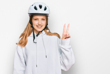 Beautiful young caucasian girl wearing bike helmet smiling with happy face winking at the camera doing victory sign. number two.