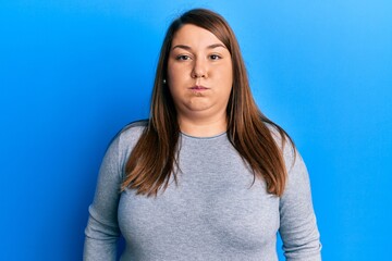 Obraz premium Beautiful brunette plus size woman wearing casual clothes puffing cheeks with funny face. mouth inflated with air, crazy expression.
