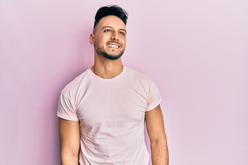 Young arab man wearing casual clothes looking away to side with smile on face, natural expression. laughing confident.