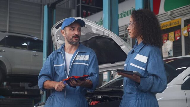 Team of mechanic with man and woman holding tablet computer in uniform talking and discussion for examining car in the garage, auto service, technician with diagnostic and checking vehicle.