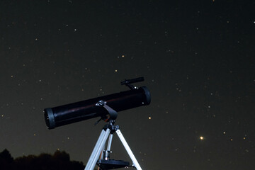 Telescope close-up under the starry dark night sky. Black reflector on a tripod.