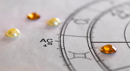Detail of printed astrology chart with orange sequinsand white pearls in the background, ascendant,...