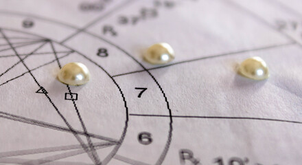 Detail of printed astrology chart with pearls in the background, marriage astrology concept