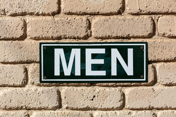 Photograph of a metal men's toilet sign on a brick wall