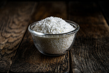Coconut shavings in a glass dish, on a wooden table.