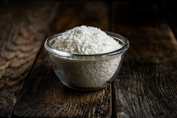 Coconut shavings in a glass dish, on a wooden table.