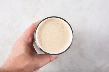 A top down view of a hand holding a glass of either cold brew coffee with a nitro head or a dark stout style beer with a full frothy head.