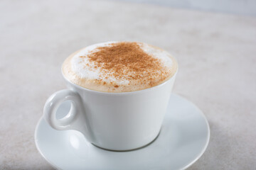 A view of a cappuccino coffee mug, garnished with foam and cinnamon.