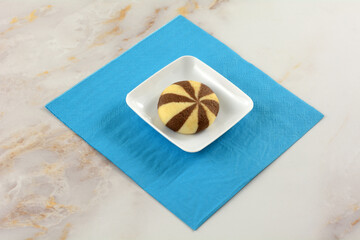 Cocoa cream swirl cookie on tiny small snack plate on blue paper napkin