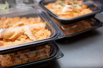 A view of stacks of entrees prepared inside to-go plastic containers, ready for take out orders, in a restaurant setting.