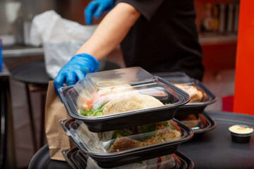 A view of an employee preparing to pack several food to-go containers, in a restaurant kitchen setting.