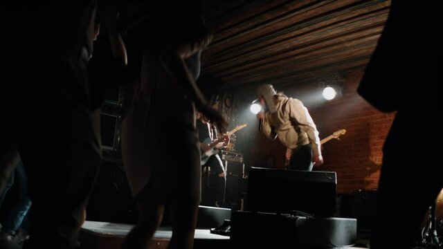 HANDHELD MED Punk rock band playing music during their concert on a stage of crowded venue. Vocals, guitars and drums. Shot with 2x anamorphic lens