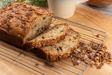 Slices cut off from a loaf of banana bread with pecan pieces baked in fresh from the oven on a wire rack 
